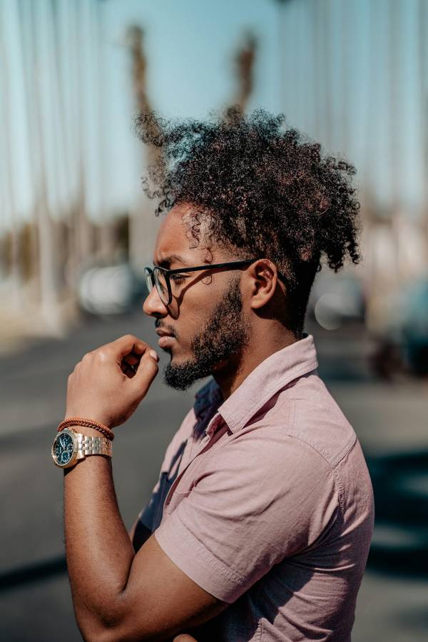 Cheveux crépus laissés en volume sur le dessus, dégradé net sur les côtés et barbe sculptée.