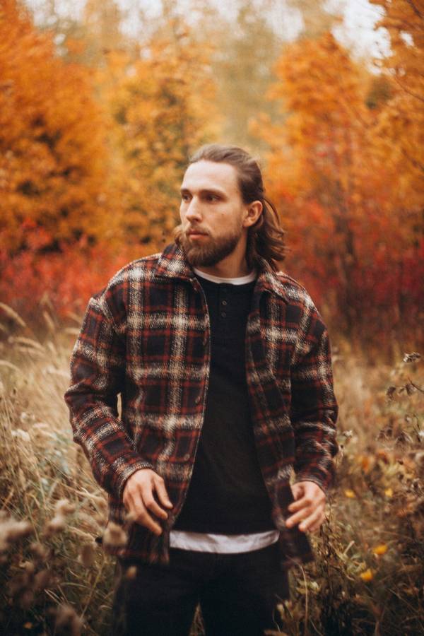 Cheveux mi-longs attachés en arrière et barbe pleine, taillée courte sur les joues.